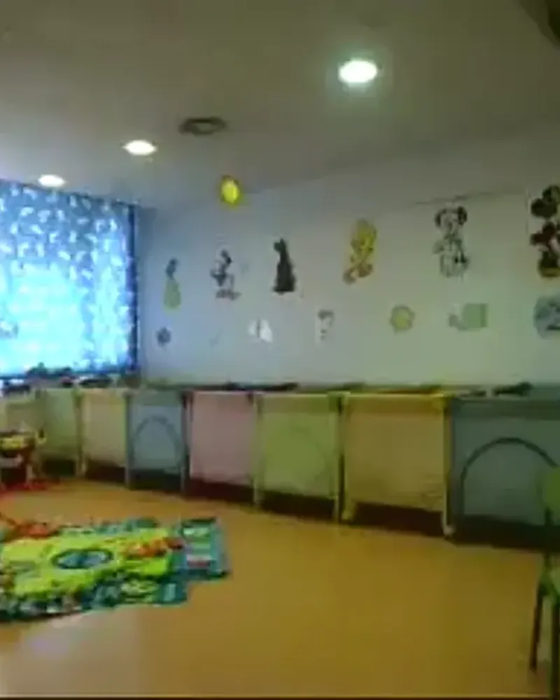 Aula de bebés de la escuela, con las cunas contra la pared y la alfombra de juego en el suelo