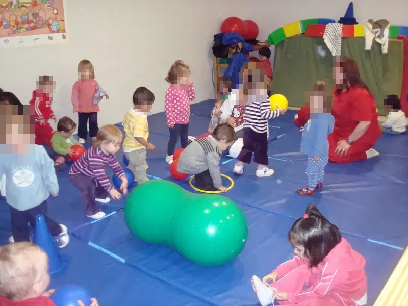 Sesión de psicomotricidad: niños pequeños con pelotas y aros sobre colchonetas